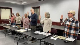 board of trustees with raised hands in front of desks for meeting